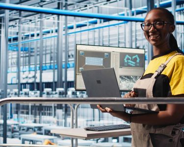Portrait of happy engineer in smart photovoltaics factory looking at system performance metrics. Cheerful worker in solar panels plant tracking energy production through IoT sensors, camera A